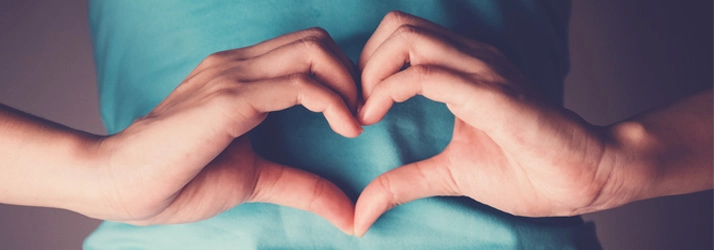 A person making heart hands over their stomache.