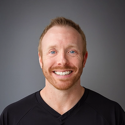 Chiropractor Michael Krueger Smiling In Front Of Grey Background In Scrubs